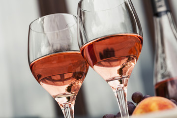 Two glasses of rose wine and board with fruits, bread and cheese on wooden table