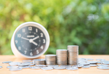Growing coin stack with clock and nature background for saving money concept