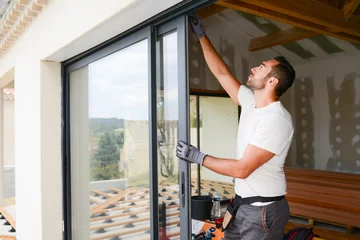 Fotobehang handsome young man installing bay window in a new house construction site © W PRODUCTION