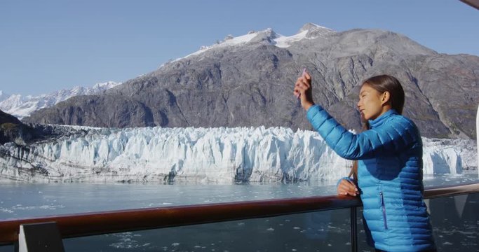 Alaska cruise ship passenger taking selfie photo in Glacier Bay National Park, USA. Woman tourist taking picture using smart phone on travel vacation. Margerie Glacier. RED EPIC SLOW MOTION.