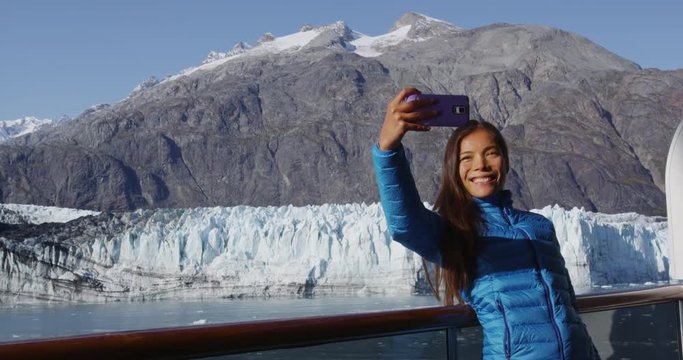 Tourist on Alaska cruise ship passenger taking selfie photo in Glacier Bay National Park, USA. Woman tourist taking picture using smart phone on travel vacation. Margerie Glacier. RED EPIC SLOW MOTION