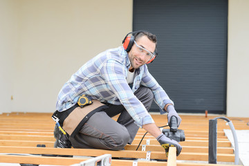 handsome young man carpenter installing a wood floor outdoor terrace in new house construction site