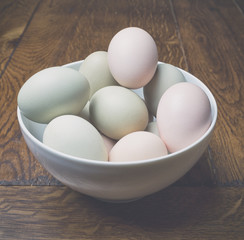 Fresh eggs in bowl on wooden table, low contrast image.
