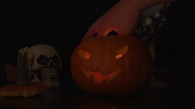 Carved Halloween pumpkin lights inside with flame and skuls around.