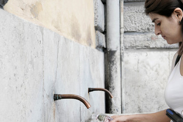 A woman Filling a bottle with drinkable water in a public fountain, Rome, Italy
