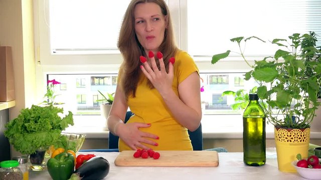 smiling pregnant woman eating raspberry berry and look at camera