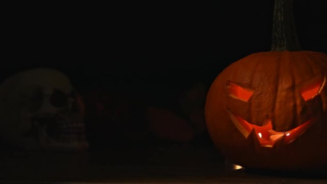Carved Halloween pumpkin lights inside with flame and skuls around.