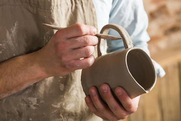 pottery, workshop, ceramics art concept - closeup on young ceramist hands with unbaked clay jug,...