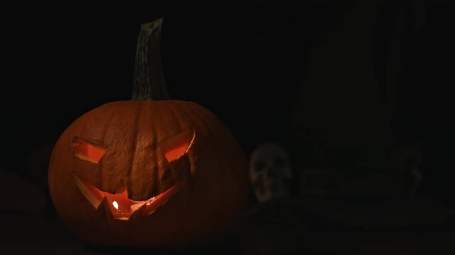 Carved Halloween pumpkin lights inside with flame and skuls around.