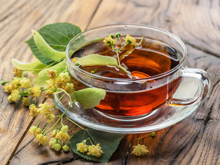 Cup of linden tea and lime flowers on the wooden table.