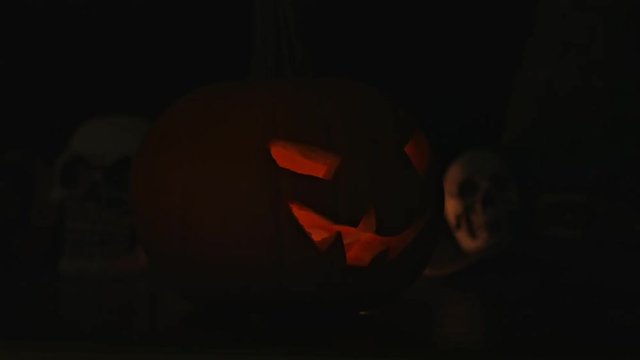 Carved Halloween pumpkin lights inside with flame and skuls around.