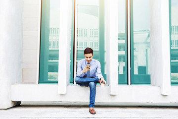 Young Businessman using or Working on a Smart Phone and sitting in outside office building, Social communicate technology in Business concept, Lifestyle of modern Male
