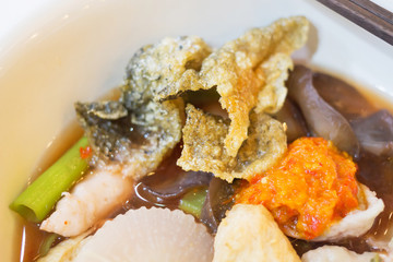Red sauce noodle soup with flat rice noodles fish balls, fish long sliced, crispy squid and crispy fish skin.