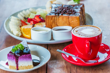 Heart latte art hot coffee in red cup, blueberry and other cake on the wooden table as love and dessert concept