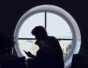 Man sitting on the window sill,using smartphone