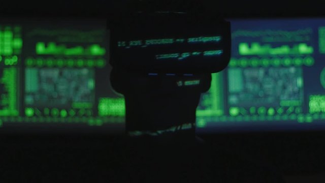 silhouette of hacker programmer uses a virtual reality helmet for programming while green code characters reflect on his face. IT Technologies of the Future.