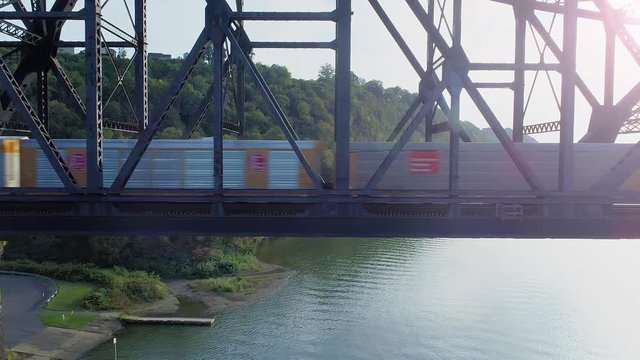 A profile aerial shot of a cargo train traveling over a railroad bridge spanning the Ohio River.  	