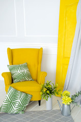 Yellow armchair in the interior with elements of home textiles, pillows and floral decor