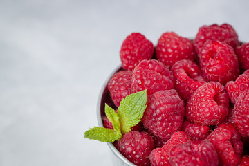 Raspberries with a mint leaf in iron bucket. Flat view. Light background