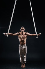 circus artist on the aerial straps making cross with Strong muscles on black background