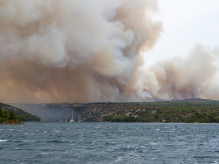 Forest fire in Croatia, summer natural disaster close to national park Krka, Sibenik region, boats and yachts escaping Skradin town from the smoke