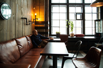 Young serious fashionable man sitting alone in loft-styled cafe. Former factory building, natural daylight.