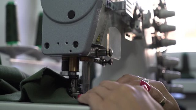 Woman tailor hands close up during works at sewing machine,female dressmaker stitches green cloth, shallow depth of field,concept tailoring, room interior