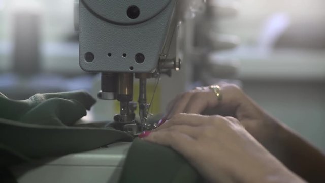 Female tailor works at sewing machine, hands of dressmaker stitches green cloth, shallow depth of field,concept tailoring, room interior, macro shot