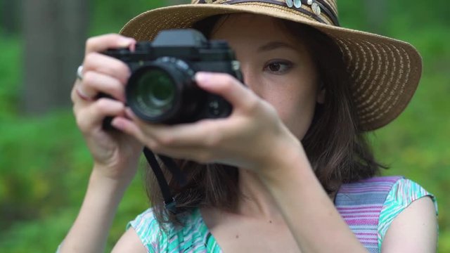young woman in dress and straw hat takes pictures of nature with retro camera.