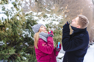 Romantic couple in love blowing bubbles, having fun together in winter clothing outdoors. Soap bubbles.