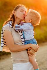 Woman and child outdoors at sunset. Boy kissing his mom.