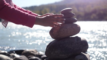 Female hands putting pebble stack next to the mountain river on sunny day