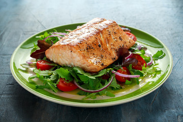 Baked salmon steak with tomato, onion, mix of green leaves salad in a plate. healthy food