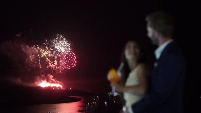 4k travel video blurred honeymoon couple in foreground amazing corlorful fireworks over island and sea at night
