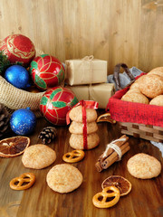 Biscuits with cinnamon in a wicker basket surrounded by present boxes and Christmas attributes on a wooden background