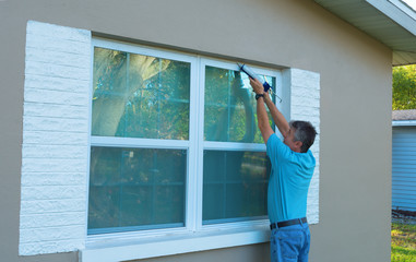 Homeowner caulking window with a caulk gun, an important part of weatherproofing homes and houses against rain, wind, hurricanes and storms.