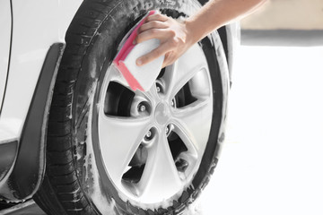 Man washing automobile wheel with sponge
