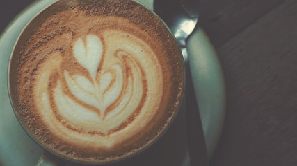 Hot cappuccino coffee with beautiful latte art on wooden coffee table, vintage color tone process and selective focus for drink background