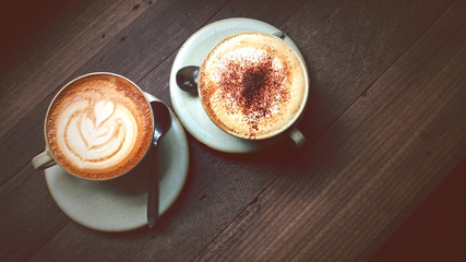 Hot cappuccino coffee with beautiful latte art on wooden coffee table, vintage color tone process and selective focus for drink background