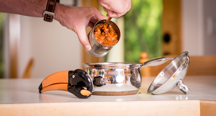 Man scoops chili out of a metal can into a pan