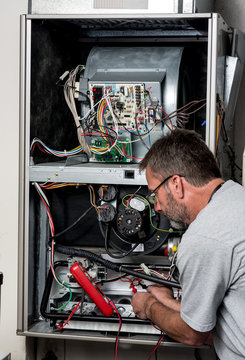 Master technician works on a home furnace with volt meter