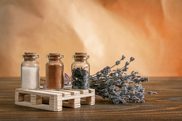 Three small jars filled with sugar, cinnamon and tea on a wooden stand with a branch of lavender on the table. Jars with spices on an orange background with empty copy space.
