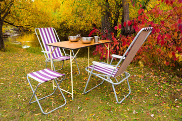 Camping table and chairs in the autumn forest on the river bank 
