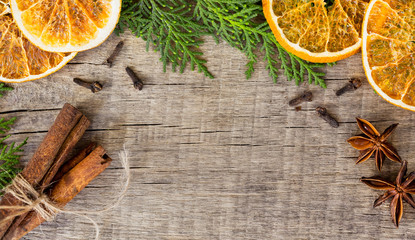On a woody background, spices are laid out: lemon, cinnamon, cloves, tubby, anise and greens cypress branches