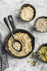 Ingredients for the preparation of baked crispy appetizing toping for thick soups puree from pumpkin seeds, sunflower seeds, oat flakes in ceramic form on a dark background. Top View.