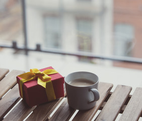 White cup of coffee or tea near a present gift