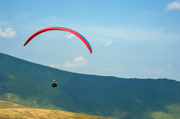 A paraglider flies over a mountain valley on a sunny summer day. Paragliding in the Carpathians in the summer.
