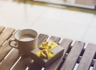 White cup of coffee or tea near a present gift