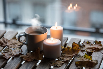 White cup of coffee or tea near candles with maple leaves