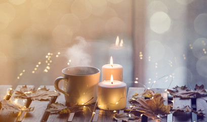 White cup of coffee or tea near candles with maple leaves